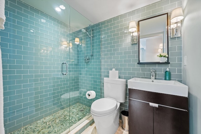 bathroom featuring toilet, a stall shower, vanity, and tile walls