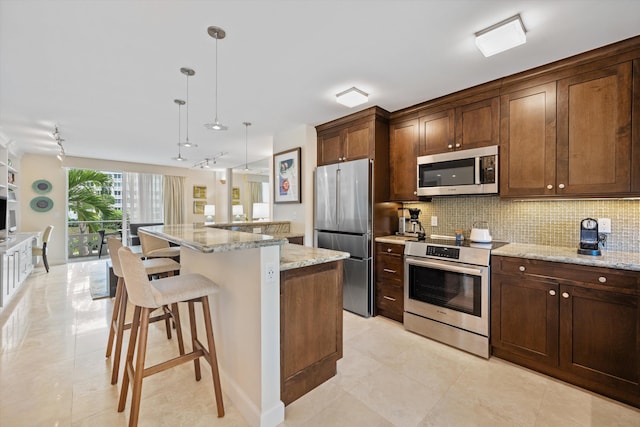 kitchen with stainless steel appliances, hanging light fixtures, a kitchen island, light stone countertops, and a kitchen bar