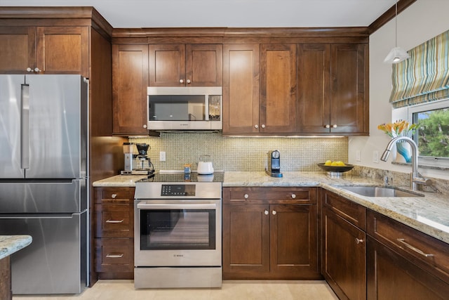 kitchen with light stone counters, tasteful backsplash, hanging light fixtures, appliances with stainless steel finishes, and a sink