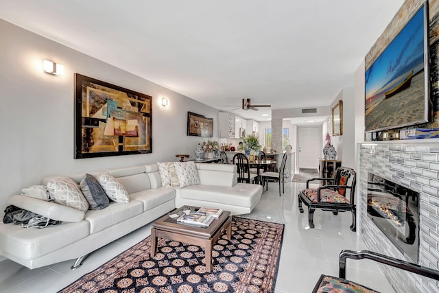 living area with light tile patterned floors, ceiling fan, a fireplace, and visible vents