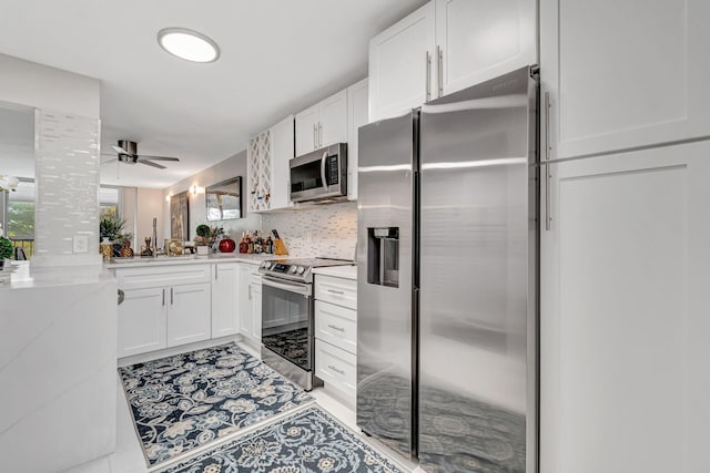 kitchen featuring light stone counters, a peninsula, white cabinets, appliances with stainless steel finishes, and backsplash