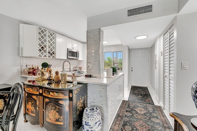 kitchen with visible vents, white cabinets, light countertops, decorative backsplash, and stainless steel microwave