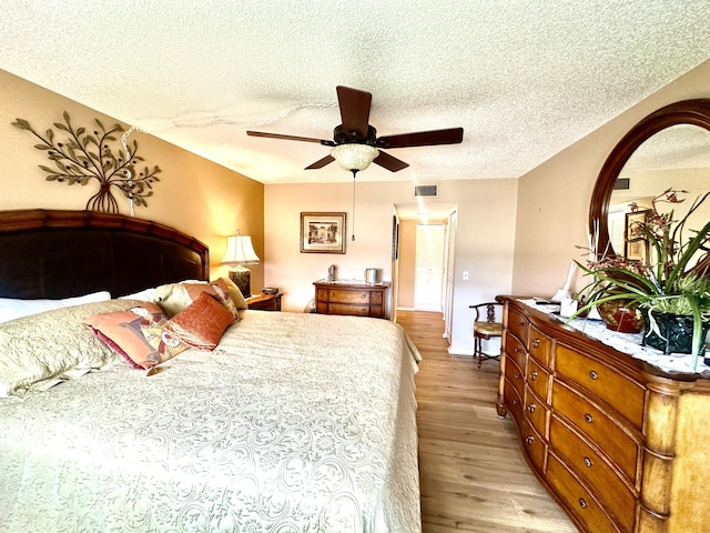 bedroom featuring light wood-style floors, a ceiling fan, visible vents, and a textured ceiling