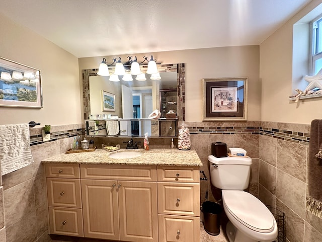 bathroom with toilet, wainscoting, tile walls, and vanity