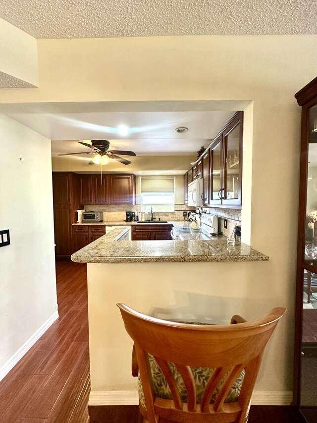 kitchen featuring light stone counters, dark wood finished floors, glass insert cabinets, a sink, and white appliances