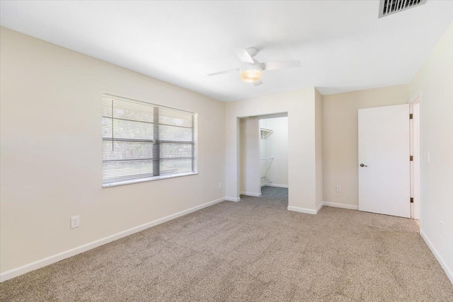 unfurnished bedroom with ceiling fan, light colored carpet, visible vents, baseboards, and a spacious closet