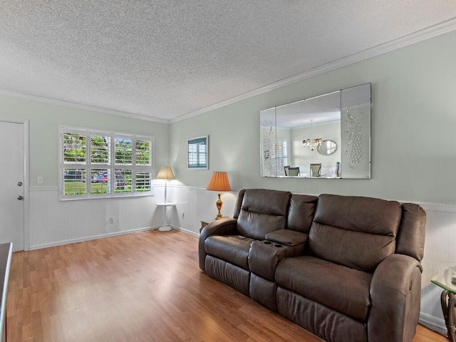 living room featuring a textured ceiling, crown molding, wood finished floors, and wainscoting