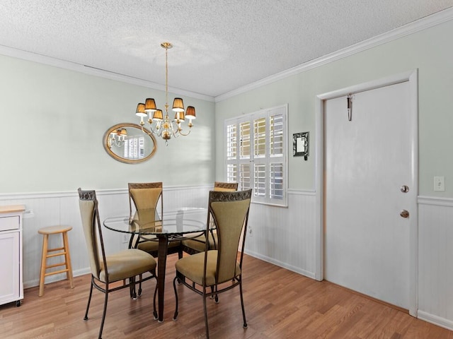 dining room featuring crown molding, light wood-type flooring, wainscoting, an inviting chandelier, and a textured ceiling