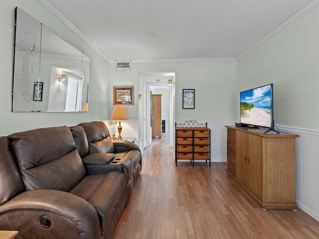 living room with visible vents, crown molding, wainscoting, wood finished floors, and a textured ceiling