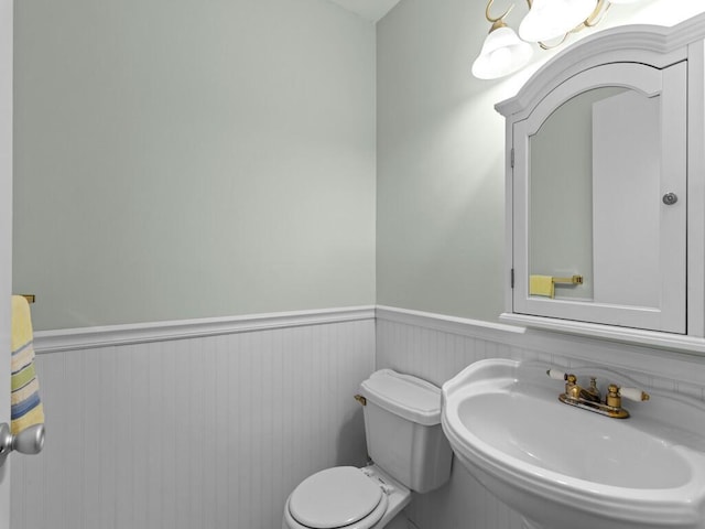 bathroom featuring a wainscoted wall, toilet, and a sink