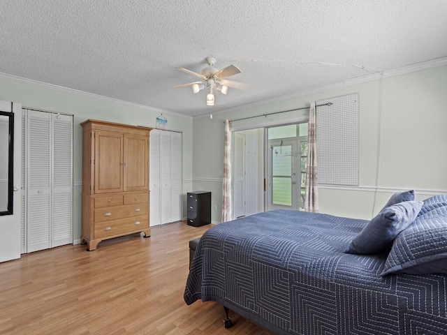 bedroom featuring light wood finished floors, two closets, a textured ceiling, and ornamental molding