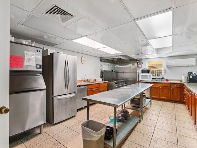 kitchen featuring visible vents, a drop ceiling, a wall unit AC, appliances with stainless steel finishes, and brown cabinetry