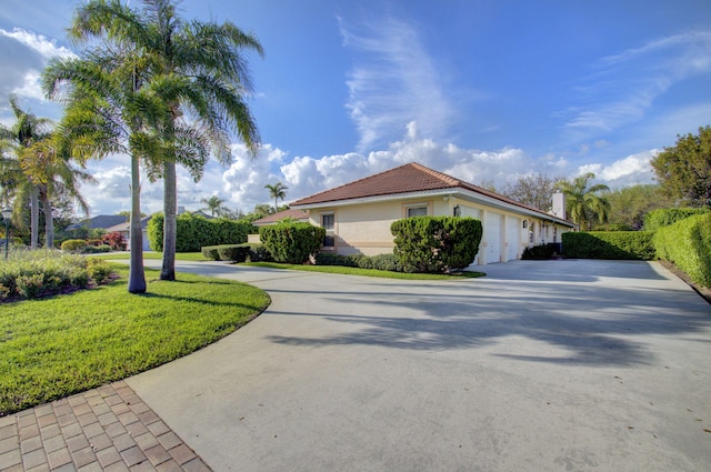 view of side of property featuring driveway, a tile roof, an attached garage, a yard, and stucco siding