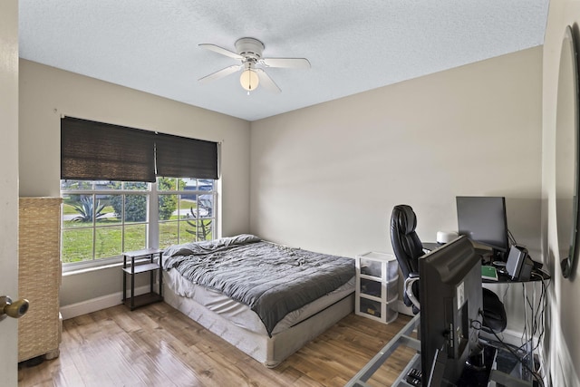 bedroom featuring light wood-type flooring, ceiling fan, baseboards, and a textured ceiling