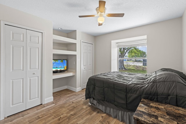 bedroom featuring baseboards, wood finished floors, a textured ceiling, multiple closets, and built in desk