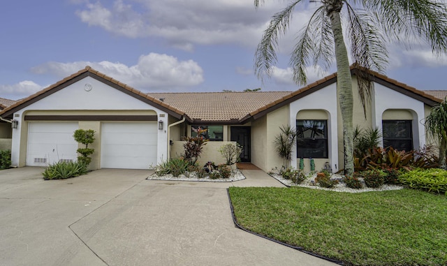 view of front of property featuring an attached garage, a tile roof, driveway, stucco siding, and a front yard