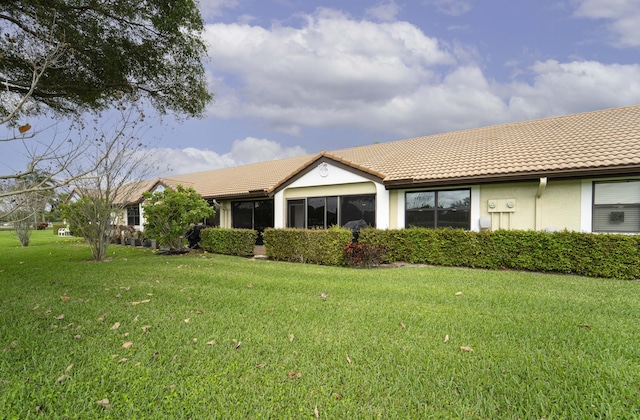 rear view of property featuring a yard, a tiled roof, and stucco siding