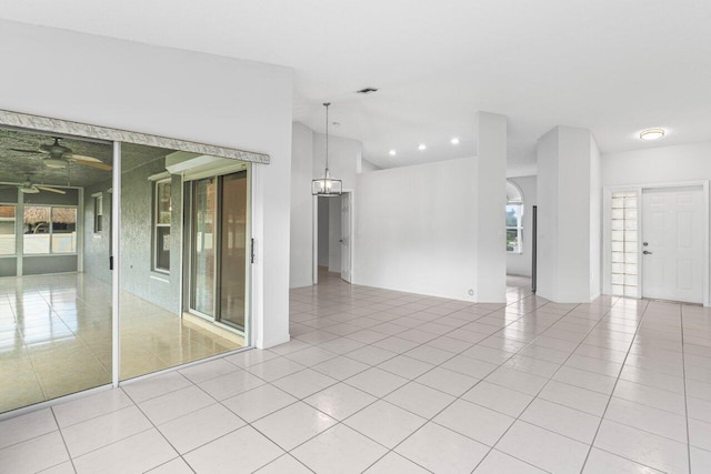 empty room with light tile patterned floors, visible vents, vaulted ceiling, and ceiling fan with notable chandelier