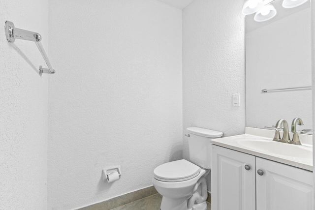 half bathroom with a textured wall, vanity, and toilet