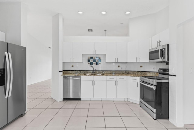 kitchen featuring light tile patterned floors, white cabinets, dark stone countertops, stainless steel appliances, and a sink