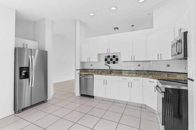 kitchen with tasteful backsplash, appliances with stainless steel finishes, white cabinets, a sink, and dark stone countertops