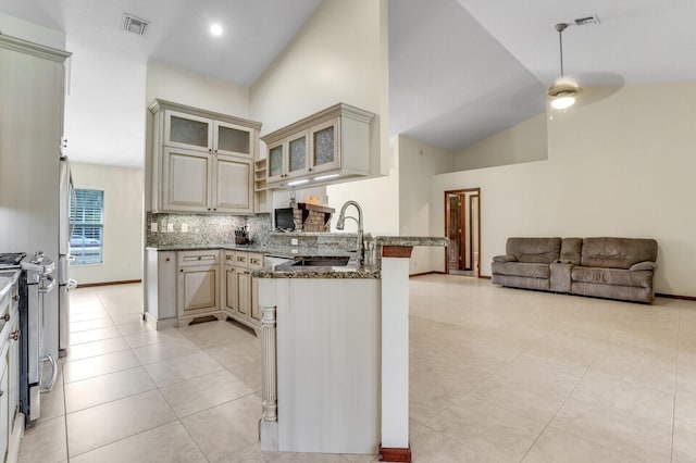 kitchen with stainless steel gas range oven, a peninsula, open floor plan, cream cabinetry, and glass insert cabinets