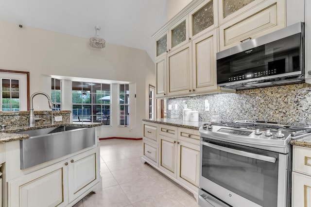 kitchen featuring light stone counters, stainless steel appliances, a sink, decorative backsplash, and glass insert cabinets