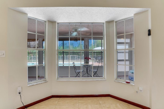 spare room featuring a textured ceiling, light tile patterned flooring, and baseboards