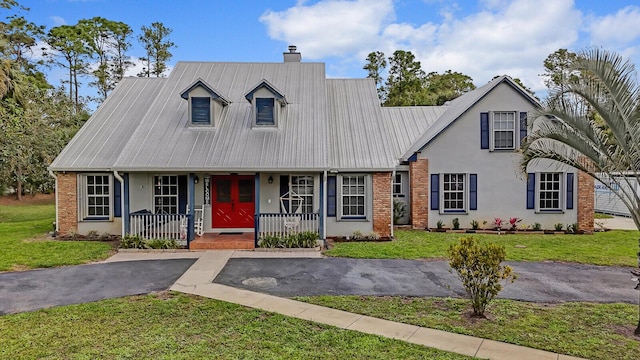 new england style home with metal roof, covered porch, brick siding, driveway, and a front yard