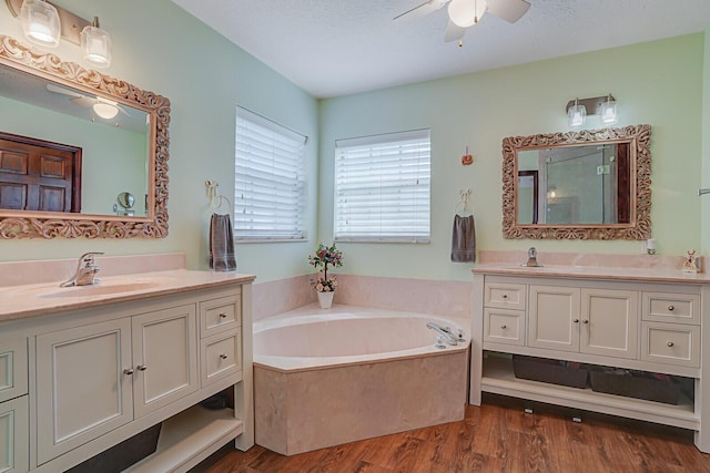 full bathroom featuring two vanities, ceiling fan, a sink, wood finished floors, and a bath