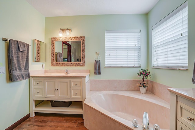 bathroom featuring a garden tub, wood finished floors, vanity, and baseboards