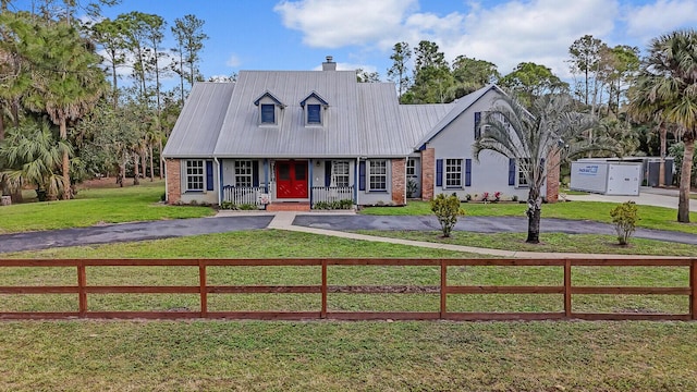 cape cod home featuring driveway, a fenced front yard, metal roof, and brick siding