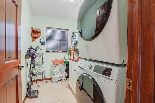 laundry area with stacked washer and clothes dryer, cabinet space, baseboards, and light tile patterned floors