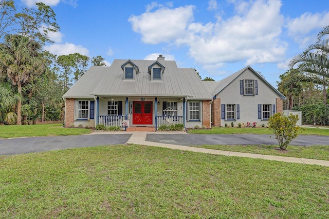 cape cod house featuring a porch, aphalt driveway, brick siding, a front lawn, and a chimney