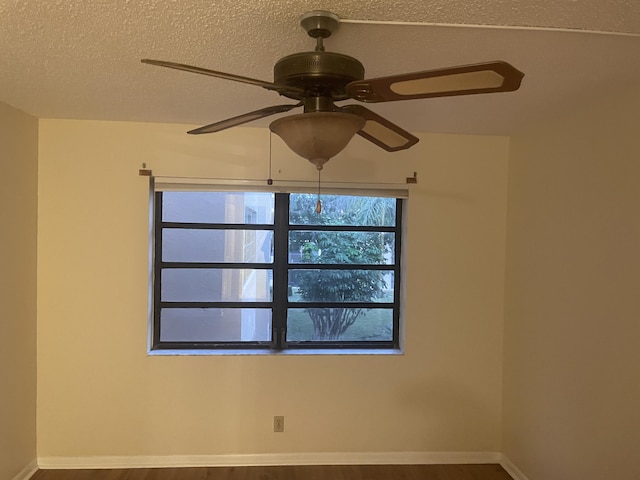 empty room featuring a textured ceiling, ceiling fan, wood finished floors, and baseboards