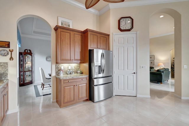 kitchen with ornamental molding, backsplash, stainless steel refrigerator with ice dispenser, and light stone countertops