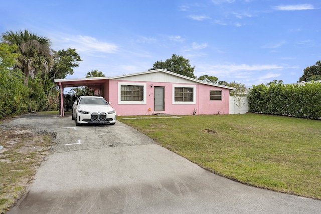 ranch-style house featuring driveway, fence, a front yard, a carport, and stucco siding