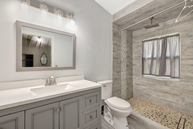 bathroom with vanity, a textured wall, a tile shower, and toilet