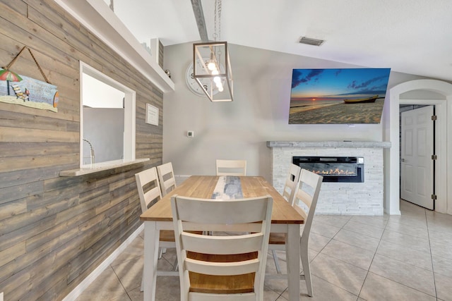 tiled dining room featuring arched walkways, wood walls, a glass covered fireplace, vaulted ceiling, and visible vents