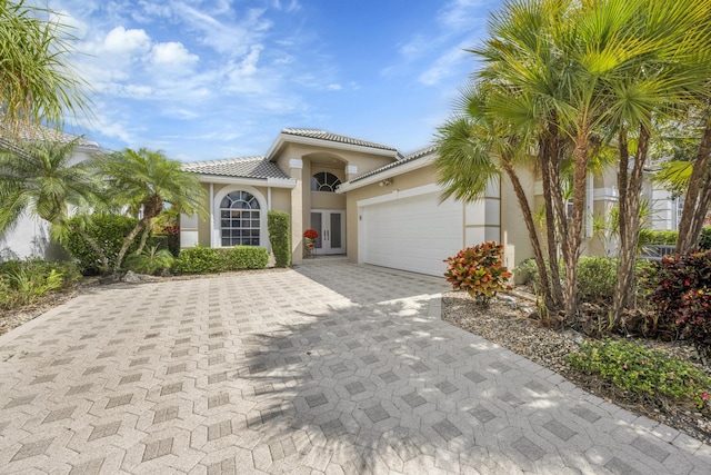 mediterranean / spanish home featuring decorative driveway, french doors, a tile roof, stucco siding, and a garage