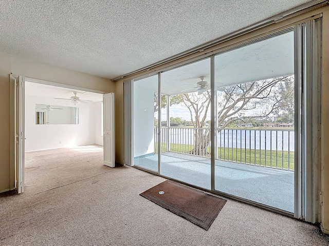 doorway to outside with ceiling fan, a water view, a wall of windows, a textured ceiling, and carpet flooring