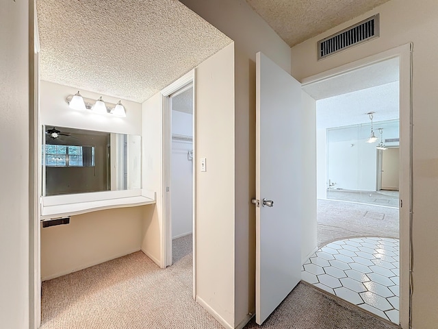 hallway with a textured ceiling, carpet flooring, visible vents, and baseboards