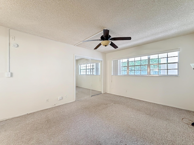 empty room featuring a ceiling fan, light colored carpet, and a textured ceiling