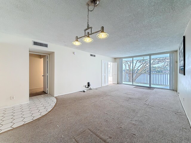 carpeted empty room with a textured ceiling, a wall of windows, and visible vents