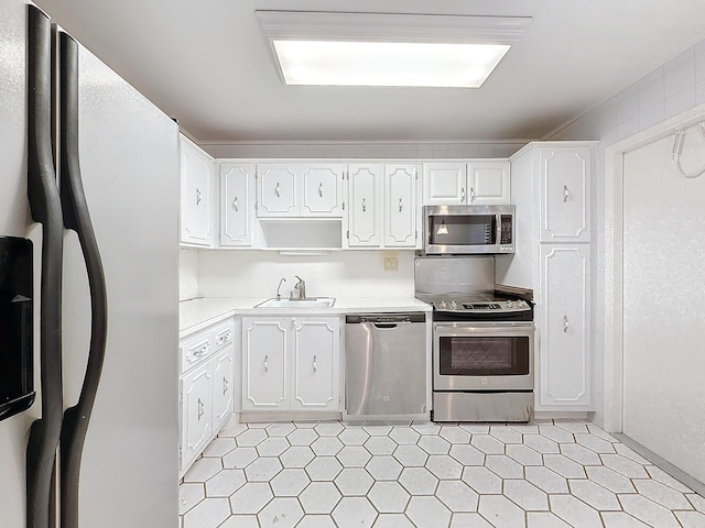 kitchen with appliances with stainless steel finishes, light countertops, light floors, white cabinetry, and a sink