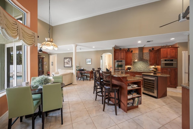 kitchen with beverage cooler, open floor plan, a center island, wall chimney range hood, and double oven