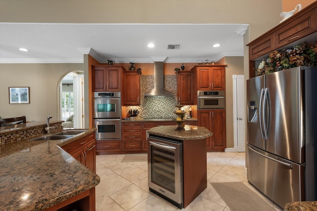 kitchen with beverage cooler, stainless steel appliances, a kitchen island, a sink, and wall chimney exhaust hood