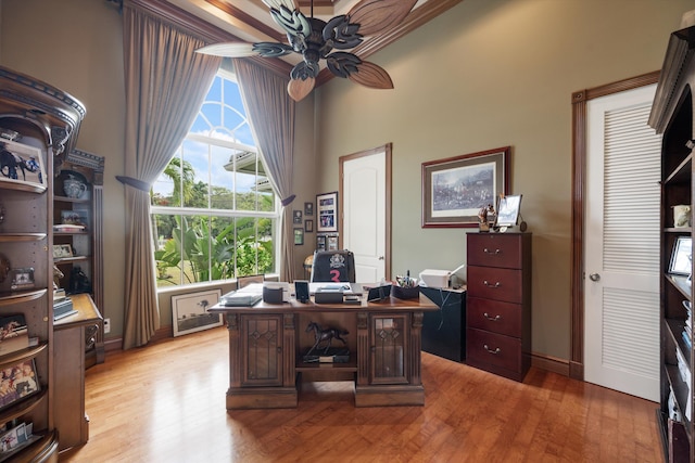 home office with light wood-type flooring, a towering ceiling, and a ceiling fan