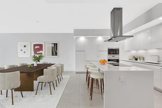 kitchen with a breakfast bar, a kitchen island, a sink, island range hood, and modern cabinets