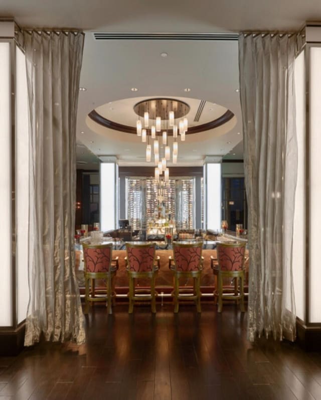 bar featuring an inviting chandelier, a raised ceiling, and hardwood / wood-style flooring